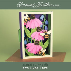 以下が含まれることがあります： ピンク色のエキナセア、緑の葉、ミツバチを特徴とする、重ねられた紙のアート作品。 作品は紫色の背景の白いフレーム内にあります。 テキスト「Furrow & Feather SVG」と「digital cutting file」が表示されています。