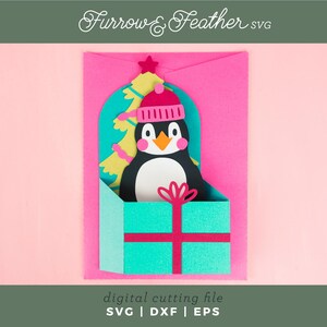 May include: A digital cutting file for a penguin wearing a pink hat and holding a Christmas tree inside a teal gift box. The file is available in SVG, DXF, and EPS formats. Furrow & Feather SVG.