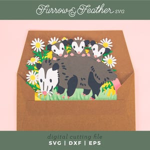 May include: A papercraft design of an opossum family in a brown envelope, with white daisies and green grass. The opossums are grey and white. The design includes the text "Furrow & Feather SVG" and "digital cutting file SVG | DXF | EPS".