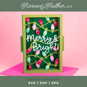 May include: A festive green card with the words "Merry & Bright" in white script, adorned with colourful Christmas lights. The card is set against a pink backdrop, with the text "digital cutting file" and file type abbreviations at the bottom.
