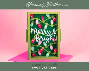 May include: A green rectangular card with the words "Merry & Bright" in white script, surrounded by colorful Christmas lights. The card is set against a pink background, with the text "digital cutting file" and file type abbreviations at the bottom.
