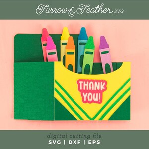 May include: A green and yellow card with a pocket for crayons. The crayons are red, orange, yellow, green, blue, purple, and pink. The card says "Thank You!" in pink letters.