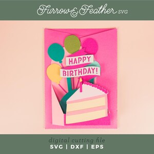May include: A pink card with a pop-up cake and balloons. The cake is white with pink icing and the balloons are green, yellow, and blue. The card says "Happy Birthday!" in pink letters.