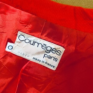 May include: Close-up of a bright red garment interior with a satin lining. A white label reads "Courr&egrave;ges paris made in france" with a small circular tag. The garment's exterior is a textured, solid red.
