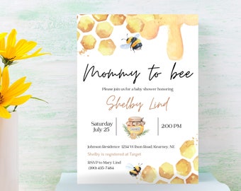 May include: A white card with a watercolor illustration of a honeycomb and a bee. The text on the card reads "Mommy to bee" and includes details for a baby shower honoring Shelby Lind. The shower will be held on Saturday, July 25th at 2:00 PM at the Johnson Residence, 1234 Wilson Road, Kearney, NE. RSVP to Mary Lind at 308-435-7484.