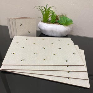 May include: Set of six beige placemats with a white polka dot pattern and a repeating design of yellow and black bees. The placemats are made of a woven material and have a slightly textured surface.