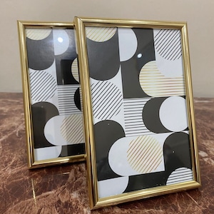 May include: Two gold-coloured picture frames with a black and white geometric pattern on the inside. The pattern features circles, stripes, and squares.