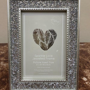 May include: A silver sparkle love jeweled picture frame with a heart design and a 6x4 inch picture insert size. The frame is ready to hang or stand.