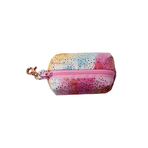 May include: A small pink and yellow pouch with a zipper closure and a gold-coloured clip. The pouch has a tie-dye pattern with gold glitter.
