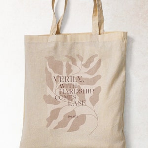 K&ouml;nnte beinhalten: Eine beige Tragetasche mit einem braunen Blattdesign und dem Text "VERILY, WITH HARDSHIP COMES EASE" auf der Vorderseite.