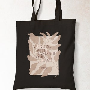 K&ouml;nnte beinhalten: Schwarze Tragetasche mit einem beigefarbenen Blumenmuster und dem Text "VERILY, WITH HARDSHIP COMES EASE [1940s]" auf der Vorderseite.