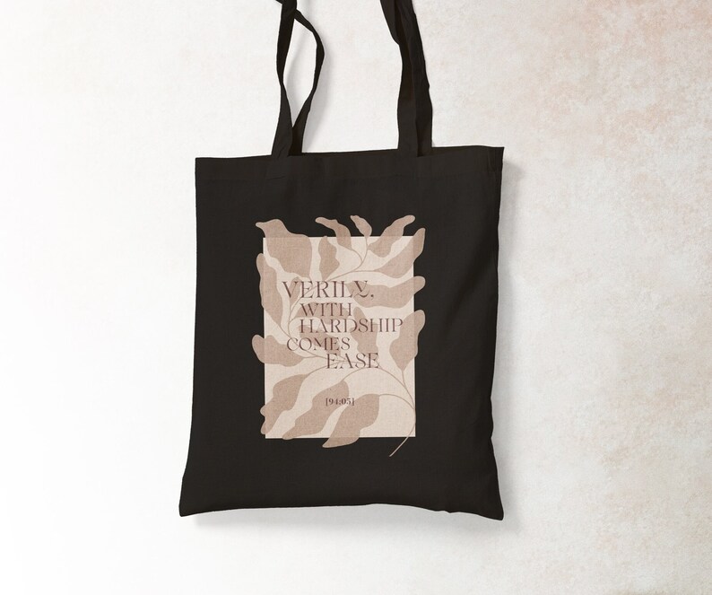 K&ouml;nnte beinhalten: Schwarze Tragetasche mit einem beigefarbenen Blumenmuster und dem Text "VERILY, WITH HARDSHIP COMES EASE [1940s]" auf der Vorderseite.