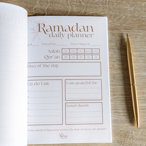 May include: A white daily planner with a brown title "Ramadan daily planner". The planner has sections for prayer times, a to-do list, and gratitude journaling. The text "in the month of Ramadan arrives, the door of mercy are opened." is printed at the bottom.
