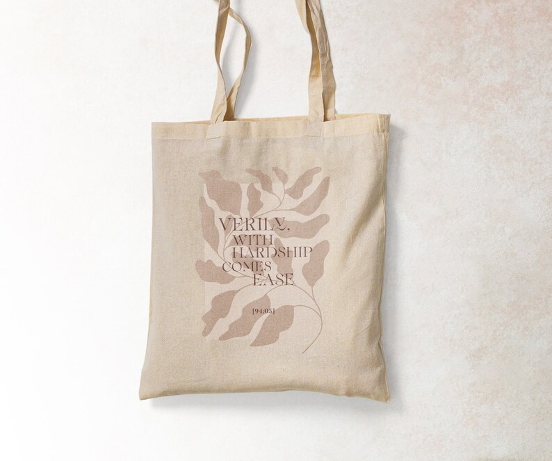 K&ouml;nnte beinhalten: Eine beige Tragetasche mit einem braunen Blattdesign und dem Text "VERILY, WITH HARDSHIP COMES EASE" auf der Vorderseite.