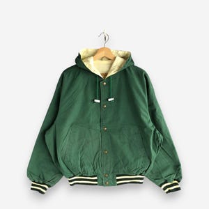 May include: A green hooded jacket with a light yellow interior. The jacket has a button-up front, a drawstring hood, and black and white striped cuffs and hem. The jacket is hanging on a wooden hanger.