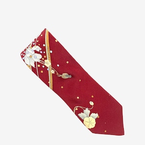 Puede incluir: Una corbata de seda roja con un estampado floral y la palabra "LEONARD" impresa en el lateral. La corbata presenta un patrón repetido de flores blancas, detalles amarillos y pequeñas formas cuadradas.