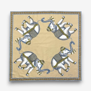 Puede incluir: Pa&ntilde;uelo cuadrado con un patr&oacute;n repetido de elefantes blancos con detalles en azul y dorado. Los elefantes est&aacute;n adornados con mantas y tocados decorativos. El pa&ntilde;uelo tiene un fondo beige y un borde azul y dorado.
