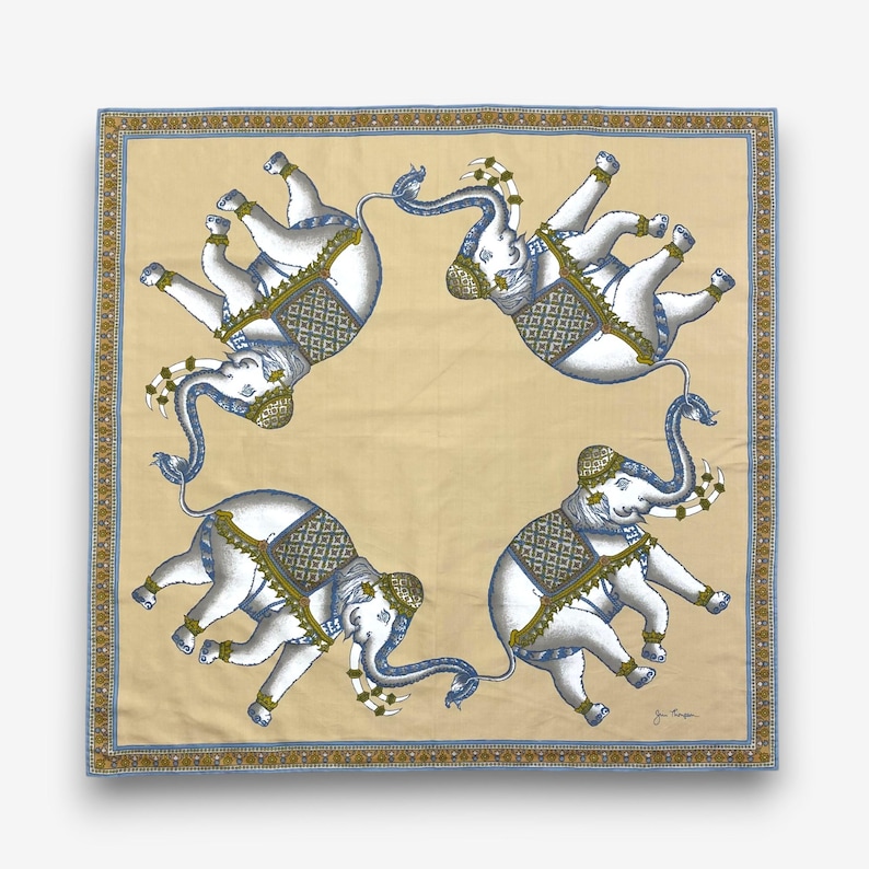 Puede incluir: Pa&ntilde;uelo cuadrado con un patr&oacute;n repetido de elefantes blancos con detalles en azul y dorado. Los elefantes est&aacute;n adornados con mantas y tocados decorativos. El pa&ntilde;uelo tiene un fondo beige y un borde azul y dorado.