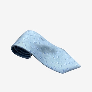 May include: Light blue tie with a repeating pattern of the letter "H". The tie is made of a smooth fabric and is angled slightly to the left. The background is plain white.