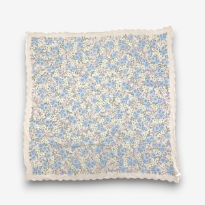 May include: A square fabric handkerchief featuring a dense floral pattern of light blue, white, and soft pink blossoms with green foliage on a cream background, finished with a delicate scalloped edge along all four sides of the textile.