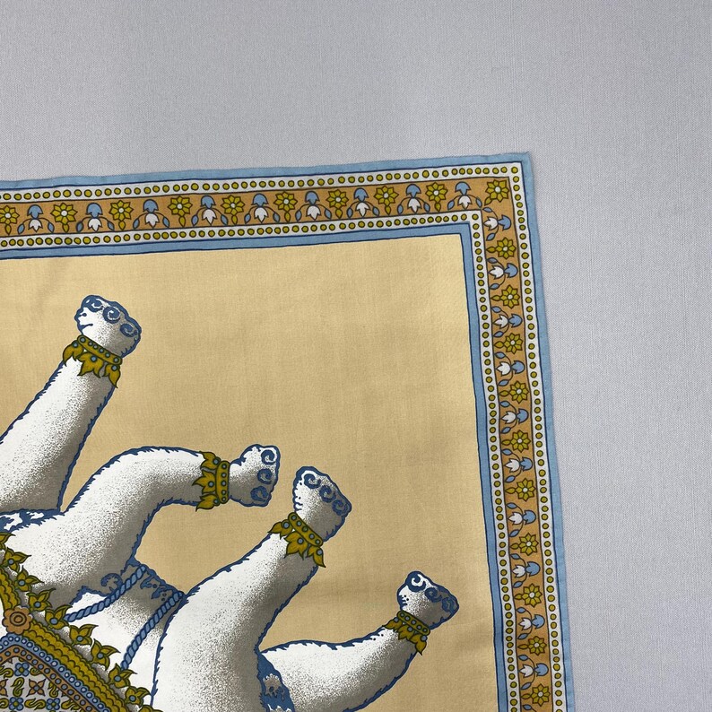 Puede incluir: Un pa&ntilde;uelo cuadrado de color crema con un dise&ntilde;o detallado. El pa&ntilde;uelo presenta un borde de patrones florales azules y dorados. El dise&ntilde;o principal incluye figuras de animales blancos con detalles en azul y dorado. El pa&ntilde;uelo tiene un borde azul claro.