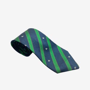 Può includere: Una cravatta a righe blu navy e verdi con piccoli motivi di cavalli bianchi ricamati. La cravatta è realizzata in un tessuto liscio ed è ben piegata, mettendo in mostra il suo motivo e il suo design.