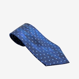 Puede incluir: Una corbata azul marino con un patrón repetido de pequeños cuadrados blancos. La corbata está hecha de una tela brillante y está inclinada hacia la izquierda, mostrando su diseño y textura. Un accesorio clásico adecuado para ocasiones formales.
