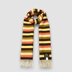 May include: A colorful striped scarf with a fringed edge. The scarf features horizontal stripes in shades of orange, yellow, brown, and cream. The scarf is made of a soft, textured material.