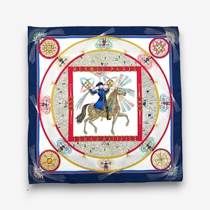 May include: Square silk scarf with a navy blue border and a central design featuring a person on horseback. The design includes red, white, and gold circular patterns, with the text "HERMES PARIS" in a red rectangle.