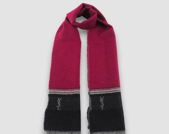 May include: A magenta, charcoal grey, and black scarf featuring a colour-blocked design. The scarf includes a thin striped pattern separating the magenta and dark sections, with the YSL logo embroidered in grey on the charcoal grey portion.