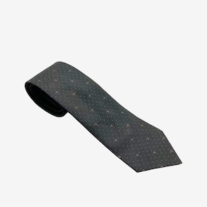 May include: A dark gray tie with a repeating pattern of small, light brown shapes. The tie is angled, showing its full length and the texture of the fabric. The tie is a classic accessory.