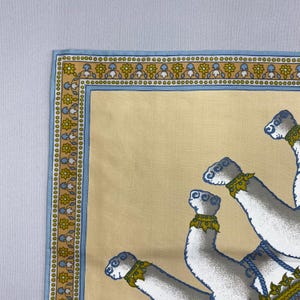 Puede incluir: Textil beige con un borde azul con un patr&oacute;n floral y de puntos. El dise&ntilde;o incluye figuras estilizadas de camellos blancos con detalles en azul y dorado. El textil tiene un aspecto suave y ligeramente texturizado.