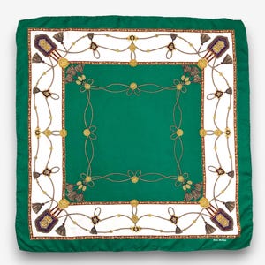 Puede incluir: Pañuelo cuadrado verde con un borde blanco con un diseño de cuerda dorada, borlas y elementos decorativos. El pañuelo tiene un centro verde liso y un borde verde oscuro. El pañuelo es de seda o satén.
