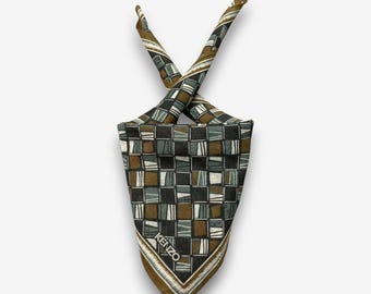 Può includere: Una sciarpa quadrata con un motivo geometrico nei toni del marrone, nero e bianco. La sciarpa è piegata e annodata, con il marchio "KENZO" visibile. La sciarpa ha un bordo tessuto.