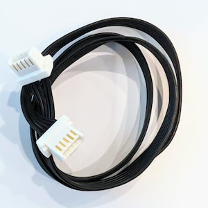 Könnte beinhalten: Ein schwarzes Kabel mit zwei weißen Steckern an jedem Ende. Die Stecker haben goldene Stifte.