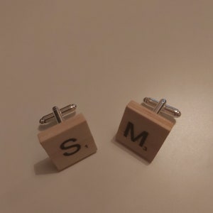 May include: A pair of cufflinks featuring wooden tiles. One tile displays the letter "S" and the number "1", the other shows the letter "M" and the number "3". The cufflinks have silver-coloured metal fittings.