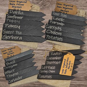 May include: A selection of black, arrow-shaped slate garden markers, laser-engraved with plant names in white. The image shows markers for flowers, herbs, and vegetables. Each set contains 6 markers.