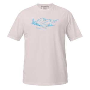 Può includere: T-shirt rosa chiaro con un disegno a tratto blu di una catena montuosa, un fiume e alberi. Il disegno è centrato sul davanti. La maglietta ha maniche corte e girocollo.