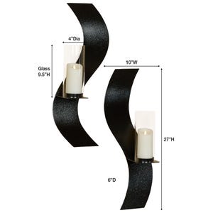 Puede incluir: Dos apliques de pared de metal negro con un dise&ntilde;o curvo y ondulado. Cada aplique sostiene un portavelas cil&iacute;ndrico de vidrio transparente con una vela de pilar blanca. Dimensiones: 68,58 cm de alto, 25,4 cm de ancho, 15,24 cm de profundidad.