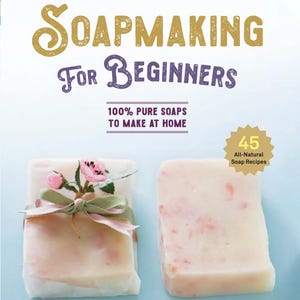 May include: A book titled Soapmaking For Beginners with the subtitle 100% Pure Soaps To Make At Home and a badge stating 45 All-Natural Soap Recipes. Below the text are two rectangular bars of soap, one wrapped with a green ribbon and pink flowers.