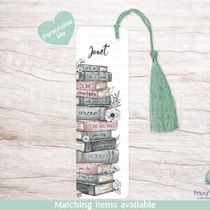 May include: A white bookmark with a stack of illustrated books, floral details, and the name "Janet". The bookmark features quotes like "Life is like a book" and has a green tassel. The words "Personalise Me" are also visible.