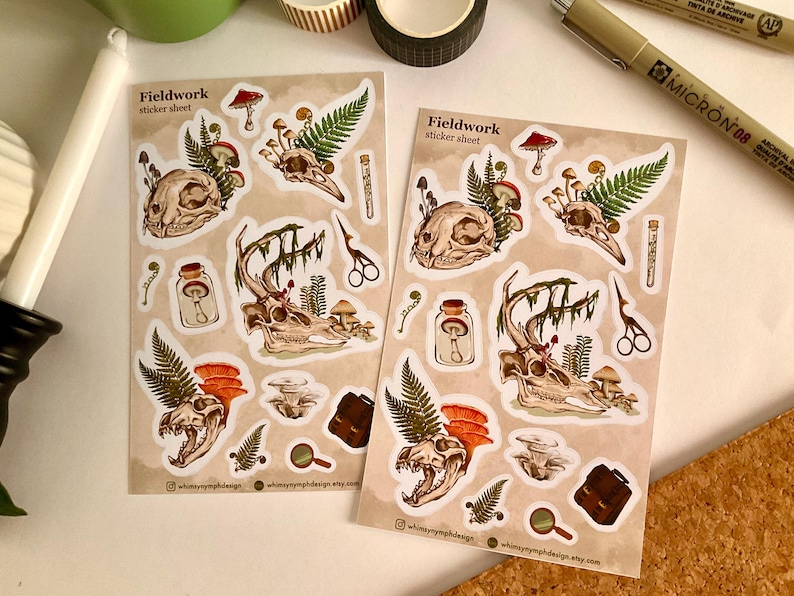 May include: Two sticker sheets with a beige background, featuring illustrations of animal skulls, mushrooms, ferns, and other botanical elements. The text "Fieldwork sticker sheet" is printed on each sheet. The stickers have a vintage, nature-inspired aesthetic.
