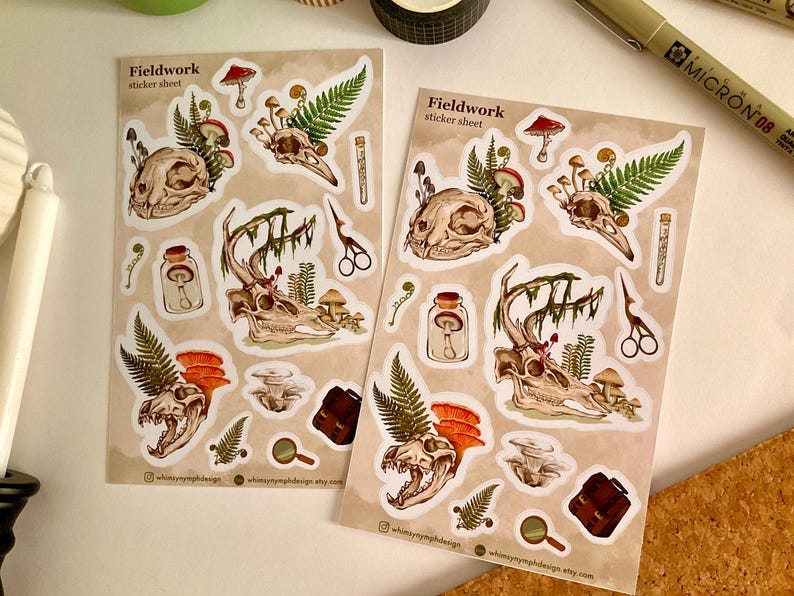 May include: Two sticker sheets with a Fieldwork theme. Each sheet features illustrations of animal skulls, mushrooms, ferns, and other botanical elements. The stickers have a vintage aesthetic with a neutral color palette and the text "Fieldwork sticker sheet".