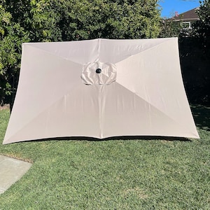 May include: A beige patio umbrella with a black center pole and a black knob on top.