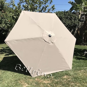 May include: A beige square patio umbrella with a black center pole and a black button on the top.