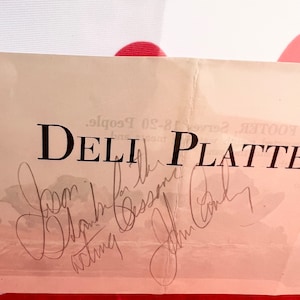 Może przedstawiać: Biała kartka z tekstem "DELI PLATTER" czarnym drukiem. Kartka jest podpisana przez cztery osoby: "Joan", "Daphne", "Danny" i "John Candy".