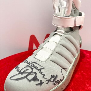 Op de afbeelding: Een witte hoge sneaker met een uniek ontwerp, met een handtekening van "Michael J. Fox".