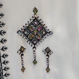 May include: A white fabric with black embroidery and iridescent rhinestones in a geometric pattern. The design features a large diamond shape with three smaller diamond shapes hanging below.