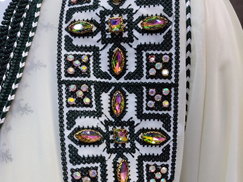 May include: A white fabric with a green and white embroidered trim. The trim features a geometric pattern with iridescent rhinestones.