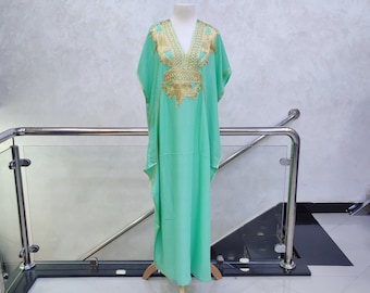 May include: A mint green kaftan with gold embroidery. The kaftan has a V-neck and short sleeves. It is a loose-fitting garment that is perfect for warm weather.